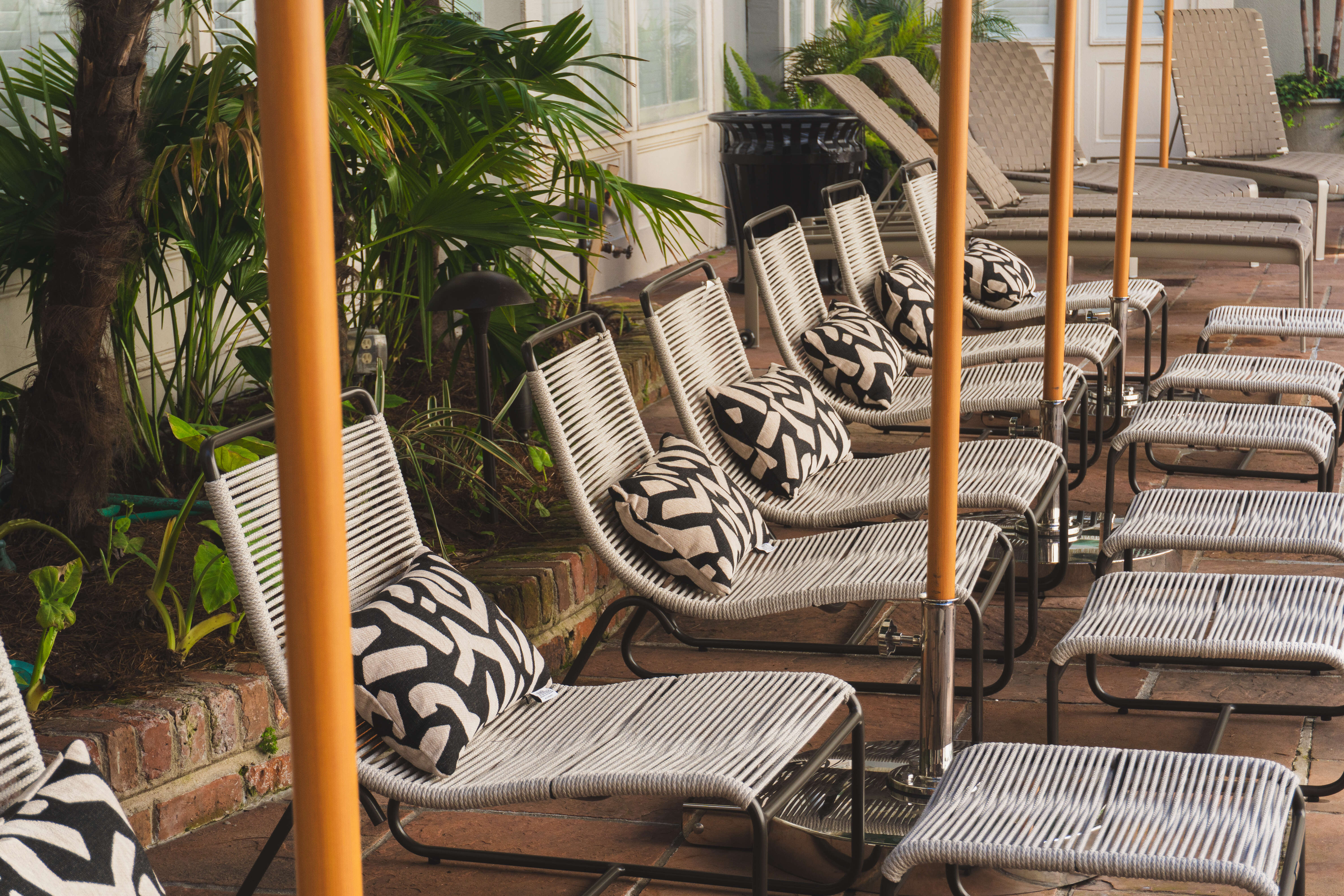 A row of lounge chairs with pillows and umbrellas by a pool area.