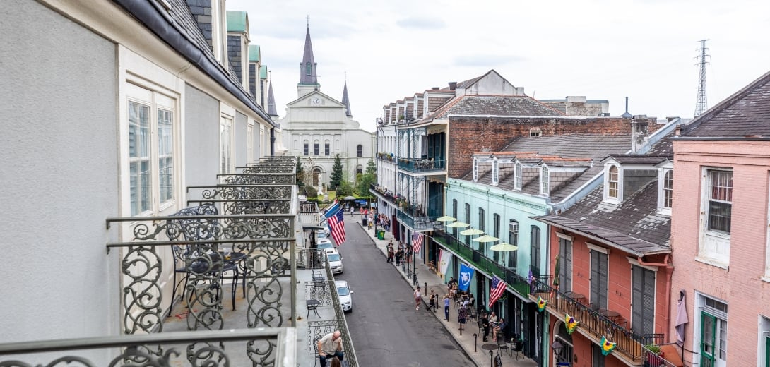 A view of a street in New Orleans from a balcony, with historic buildings, flags, and a church steeple in the background.