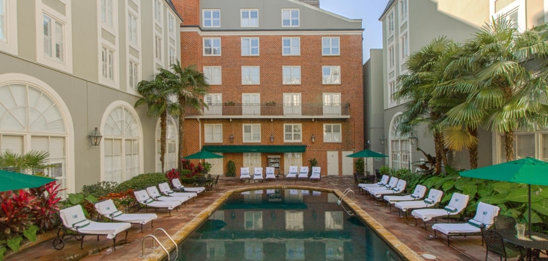 A pool with lounge chairs and umbrellas in front of a multi-story building.