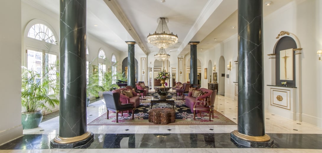 A spacious lobby with a seating area, columns, and chandeliers.