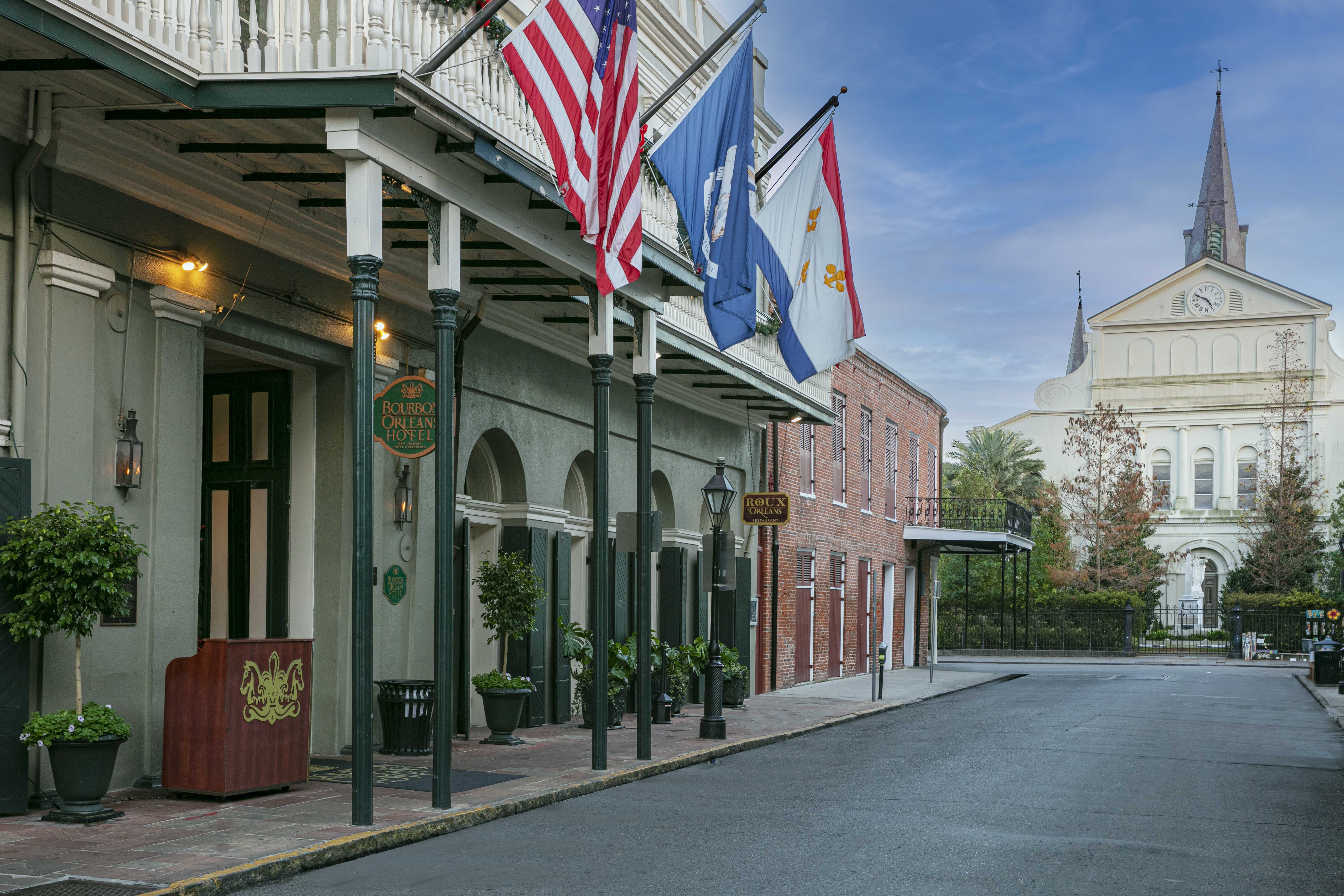 A street view of the Bourbon Orleans Hotel with flags and a historic building in the background.