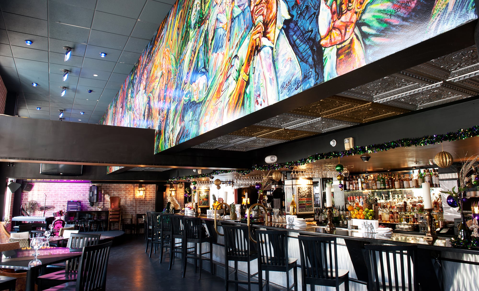 A wide view of a bar with a large mural on the ceiling