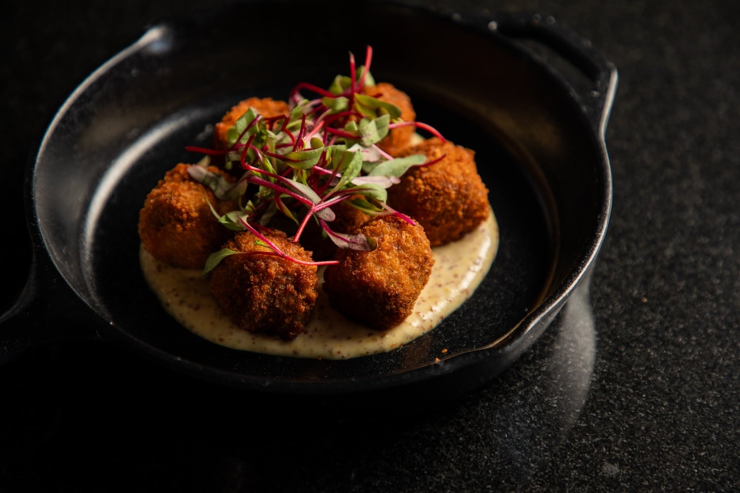a plate of fried food with microgreens and sauce