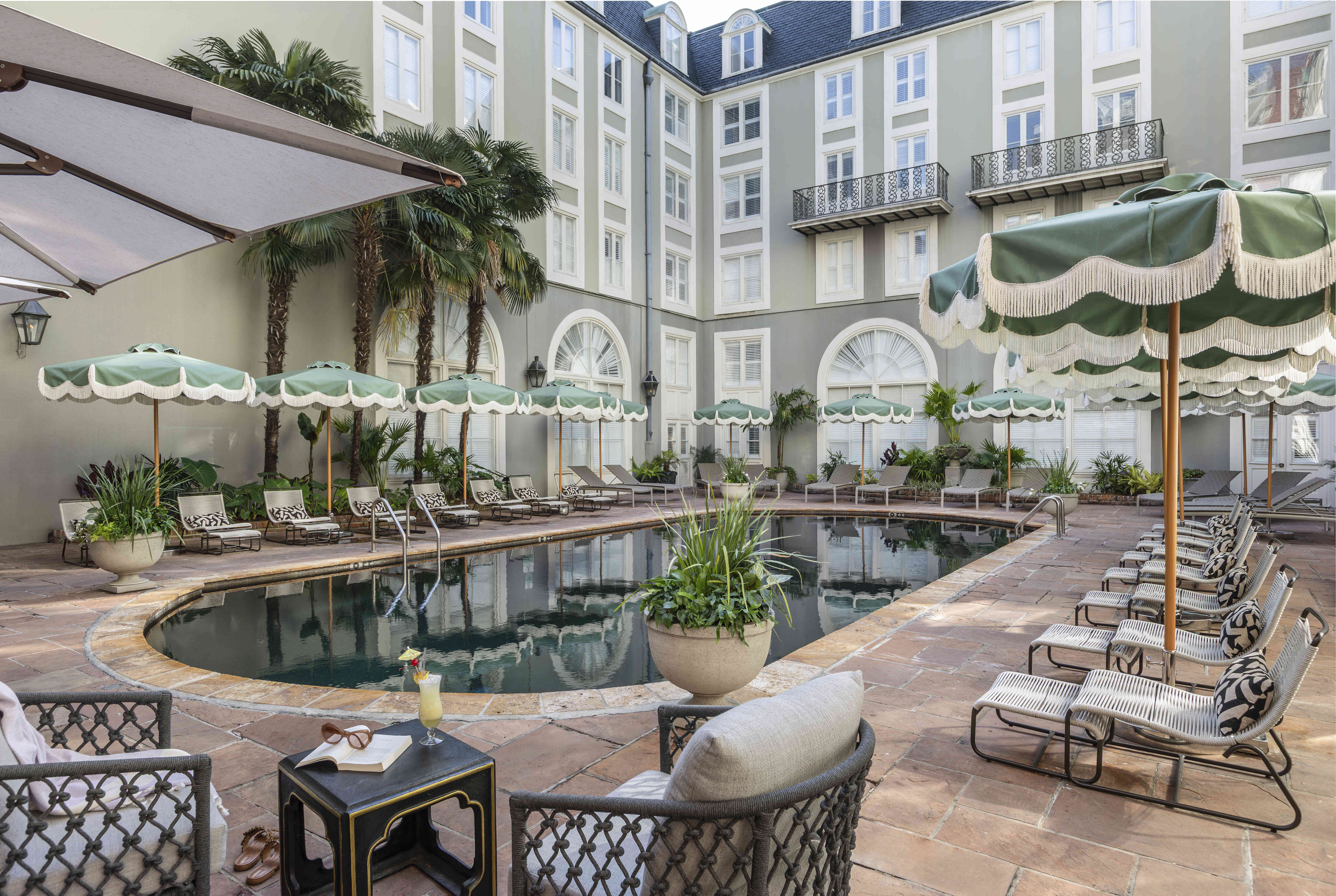 A pool area with lounge chairs, umbrellas, and a building in the background.